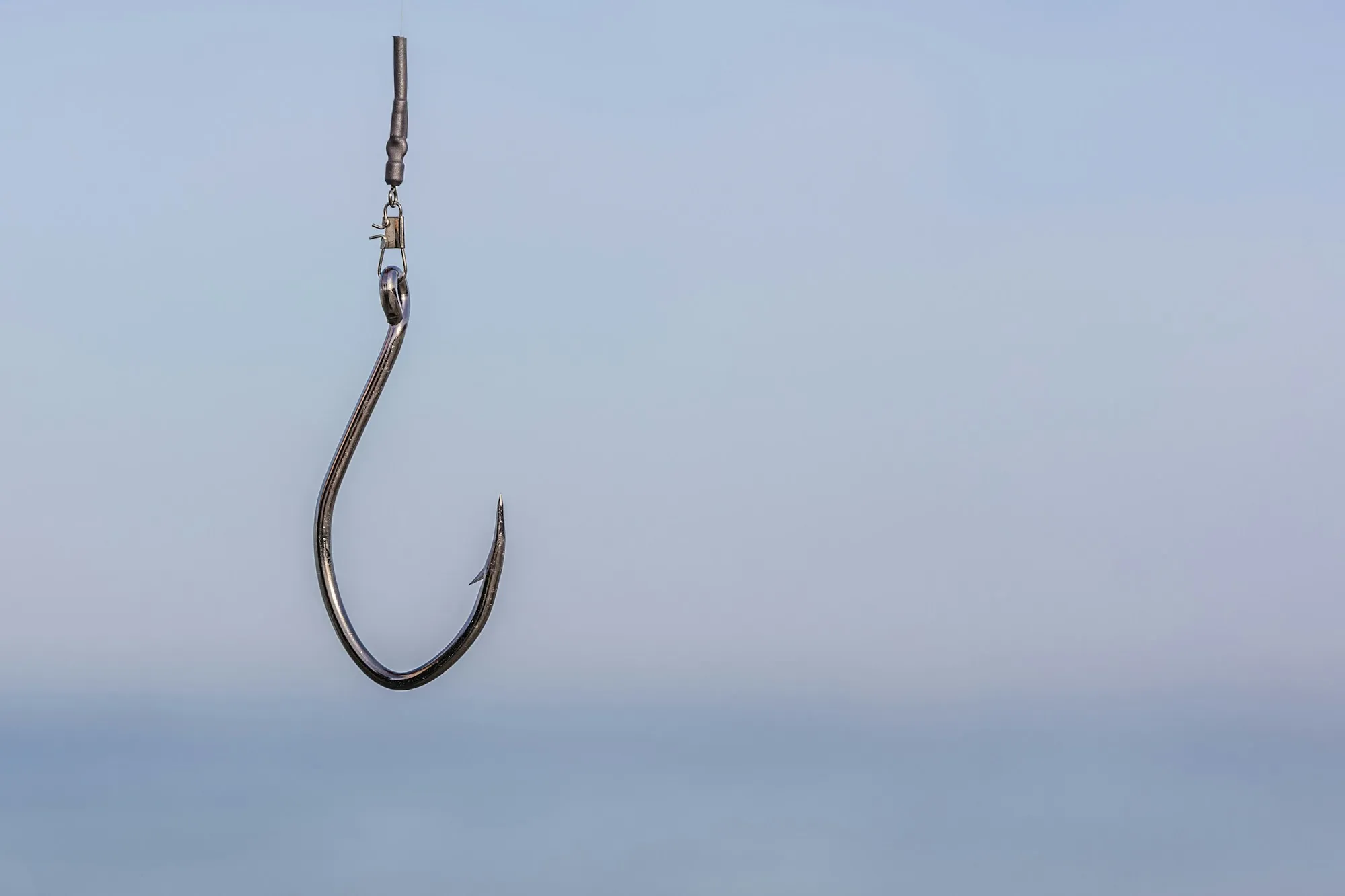 Einzelner Angelhaken hängt an einer Schnur vor hellem Himmel, am oberen Ende ist die Knotenverbindung zu erkennen
