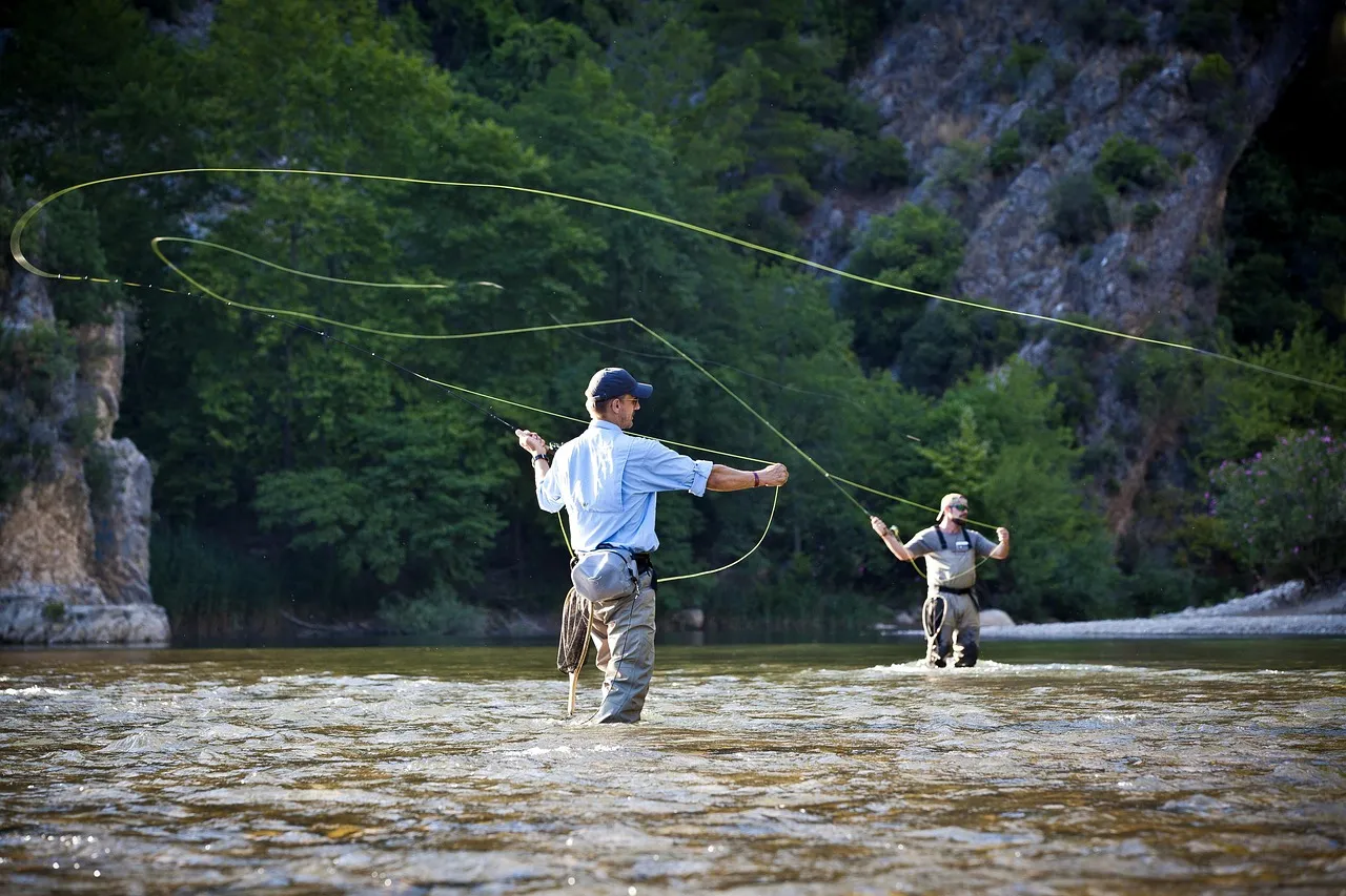 Zwei Angler waten in einem Fluss, die Fliegenschnur zieht beim Wurf eine große Schlaufe durch die Luft