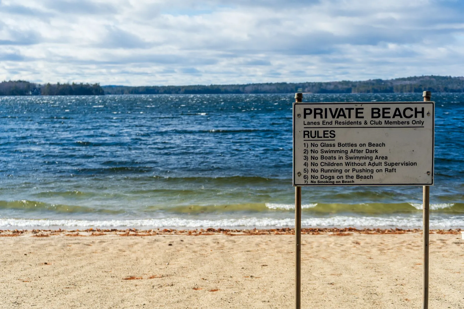 Schild mit einer englischsprachigen Regelliste steht am Sandstrand eines Sees