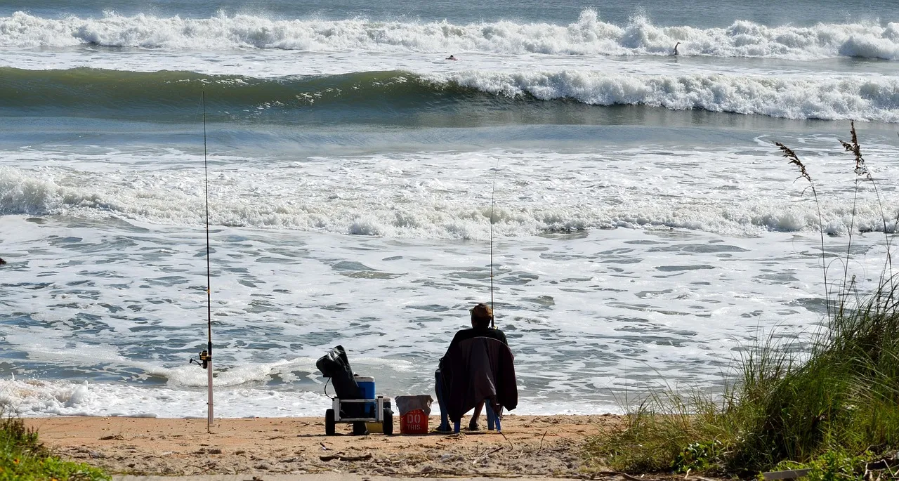 Angler sitzt am Sandstrand vor der Brandung, zwei Ruten stehen in Rutenhaltern