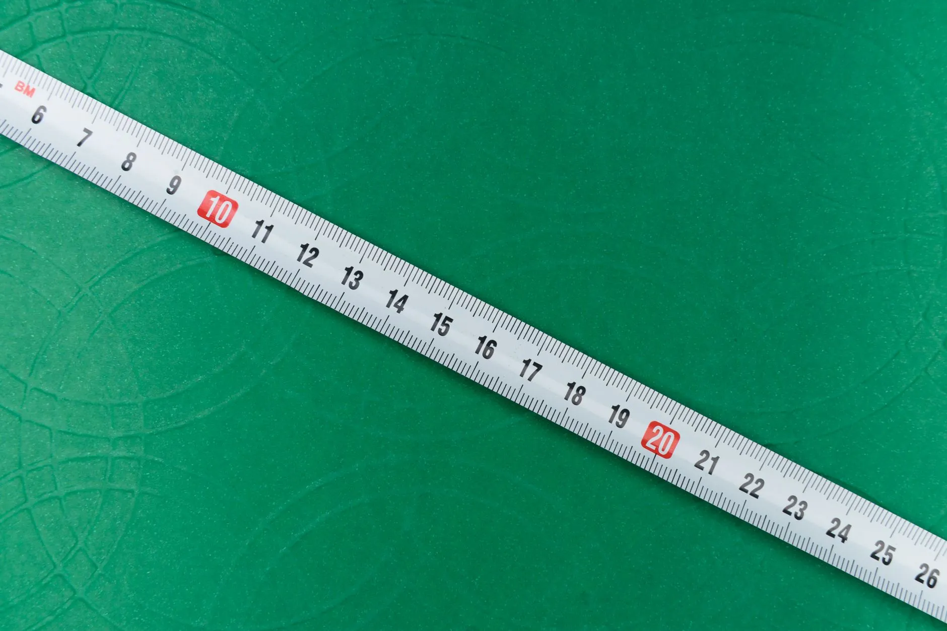Weißes Maßband mit Zentimeterskala liegt diagonal auf grünem Untergrund